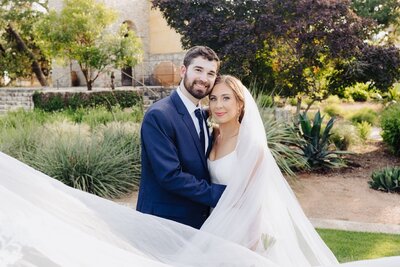Bride and groom embracing in a garden with a flowing veil, captured during a romantic Hill Country wedding planned in Austin, TX.