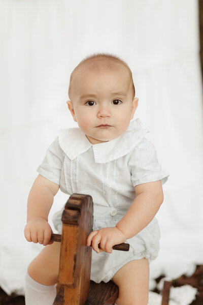 Baby boy in heirloom outfit on wooden rocking horse by Lawnreceville Heirloom Portrait Photographer
