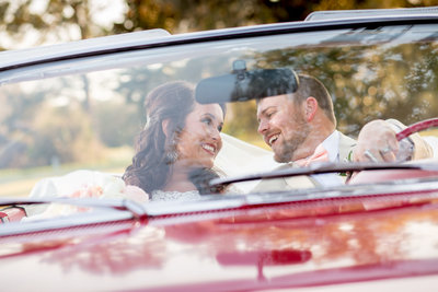Newlyweds smile in a red car on their wedding day