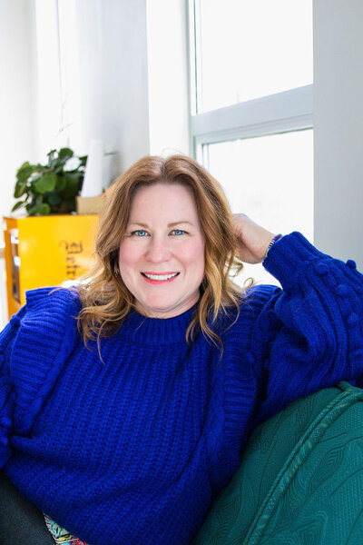 Melissa Griffin in royal blue sweater on a blue couch