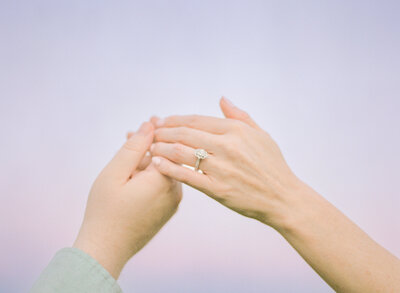 A bride and groom stand closely under a large tree, gazing at each other with smiles. The bride holds a bouquet, wearing a long lace veil. Black and white.