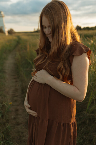 woman holds pregnant belly next to beach in pei