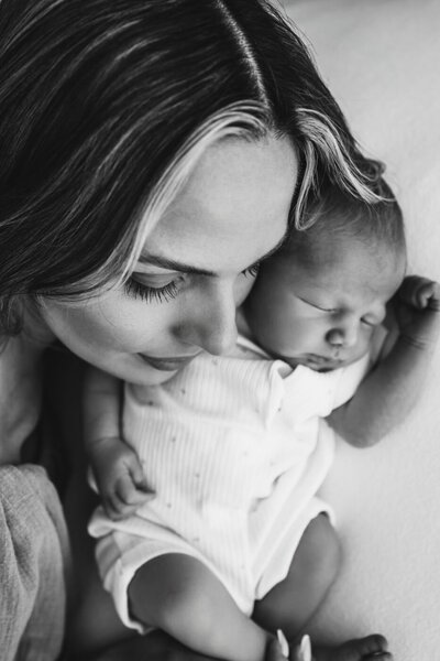 Black and white photo of a mother gently touching her forehead to her sleeping newborn baby's head.