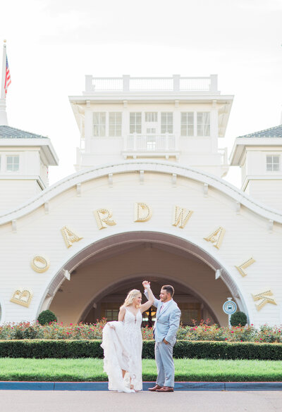Groom twirling a bride while she holds her wedding gown in front of Disney's Boardwalk Resort on their wedding day.