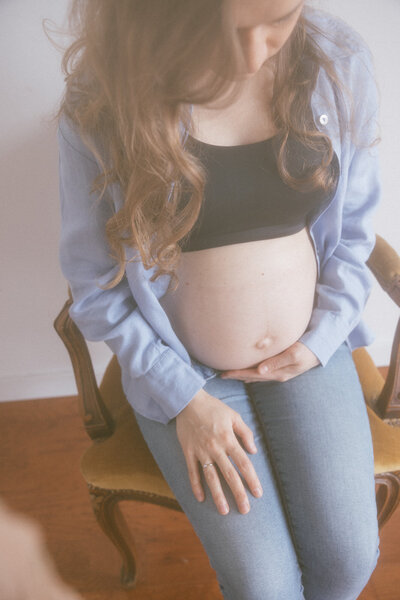 Pregnant woman in blue sits while holding her pregnant belly in a studio in Corvallis, OR.