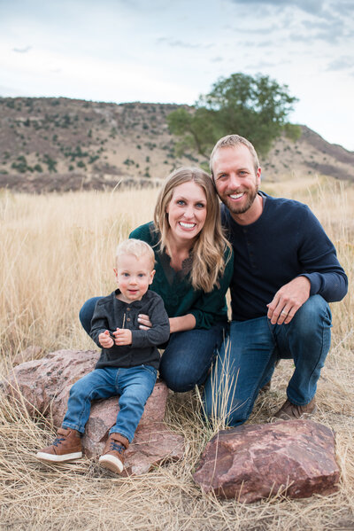 denver photographer captures outdoor family photos with mother holdin ga toddler and leaning into the dad with mountains in the distance for fall family photos