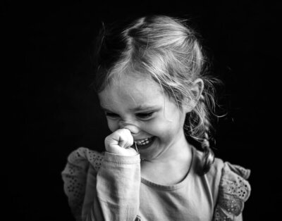 A preschool aged girl looks off to camera left giggling in a fine art black and white portrait captured on her school photo day in Minnesota.