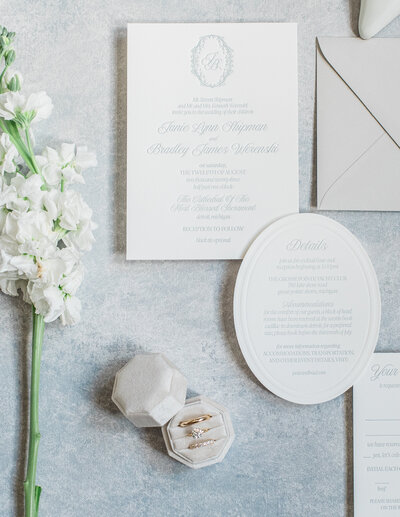 A black and white custom wedding invitation suite featuring a debossed invitation with wedding rings on it and a details and RSVP card by alyssa amez design custom wedding stationery and signage designer against a white background.