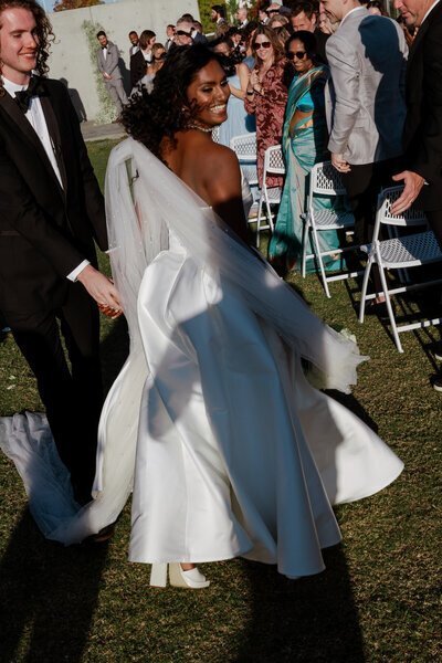 Bride smiling walking down the aisle by candid wedding photographer Noble Photo Co
