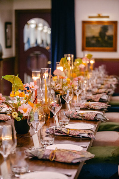 Long dinner table set for an intimate wedding reception, decorated with candles, floral arrangements, and elegant tableware in a dimly lit venue.
