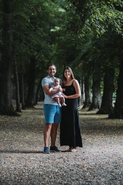 A father, mother and their baby daughter standing in the woods in Hampstead Heath, London