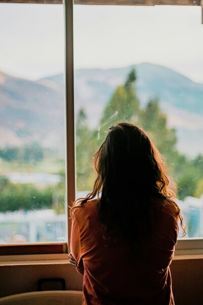 Woman looking out a window towards greenery 