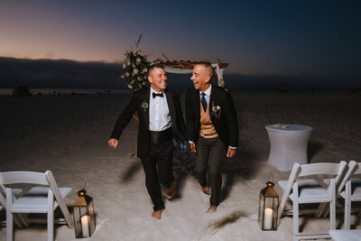 two grooms holding hands while smiling at each other