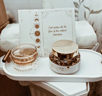 A soft tea moment unfolds with a teacup and teapot resting on a tan cushion, surrounded by white fabric and light.