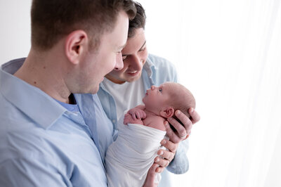 Two dads holding their newborn baby.