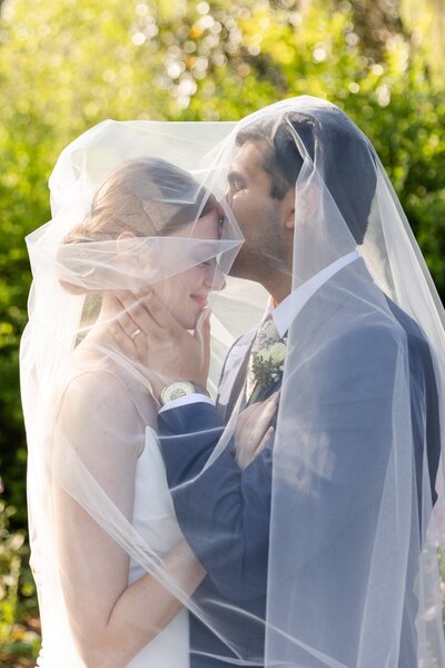 groom kissing bride on the head while they are under her veil