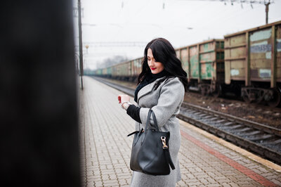 girl standing on train platform in grey jacket checking her watch for the time