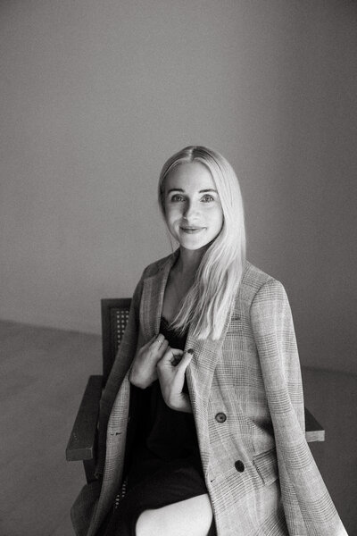Black and white photo of Fallon Stovall sitting in a chair holding a blazer over her shoulders
