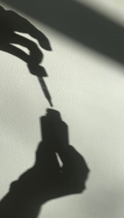 Shadow of a hand holding a dropper for liquid supplements, highlighting precision and wellness at Love Light Wellness Kauai