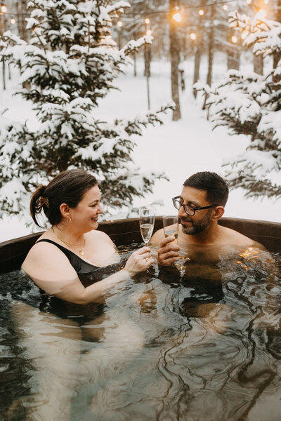 A couple enjoying the winter season with some wine, while relaxing in an outdoor hot tub at Chalets Prunella No. 1, Quebec.
