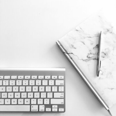 A keyboard on a desk with a journal and pen.