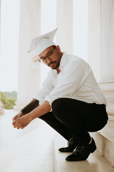 A local Washington D.C. Graduate squatting down with his hands on his knees on his campus