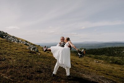 Brudgum lyfter bruden med fjäll i bakgrunden.