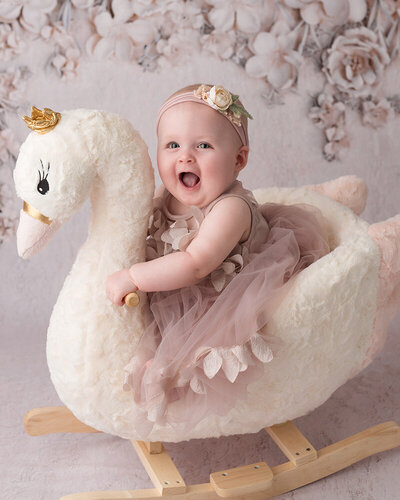 Happy smiling baby girl photographed riding a swan prop at her milestone session with Laura King Photography
