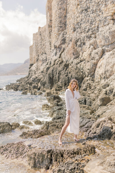 Bride in stunning wedding dress leans against stone wall in Greece