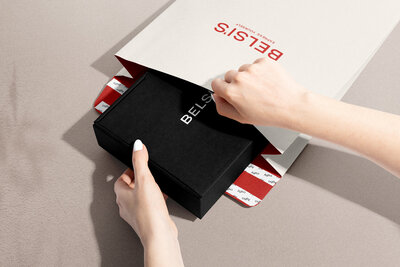 A black mailer box is being pulled out of a cream mailer envelope to show the branding design and logos for an eCommerce  jewelry brand.