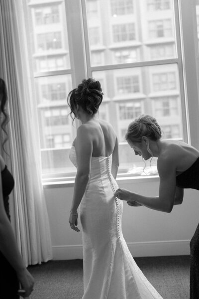 A bridesmaid helps bride into dress before her wedding day.
