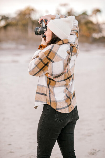 Behind the scenes photo of photographer in flannel and beanie while photographing a session in Folly Beach South Carolina