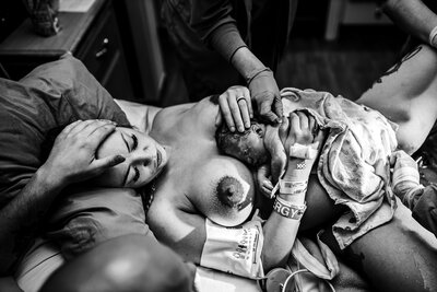 DFW birth photographer capturing an emotional black and white moment of a mother holding her newborn right after birth.