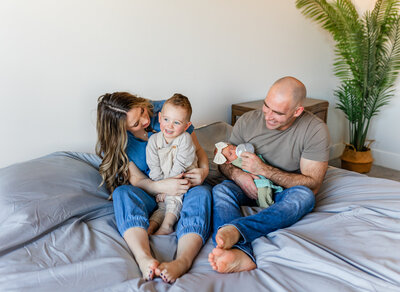 family sitting on bed and snuggling with their toddler and newborn baby