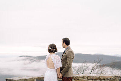 Bride holding a wildflower bouquet and gazing into the distance during her Virginia mountaintop elopement, captured in soft, editorial light with a film-inspired look.

