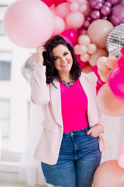 Jessi Cabanin holding a pink planner notebook sitting at a desk with a laptop and boss babe coffee cup on it.