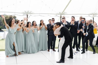 A wedding couple kissing on the dance floor with their wedding guests celebrating behind them 