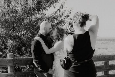 A black and white image of Em, the photographer, photographing a Bride & Groom touching noses.