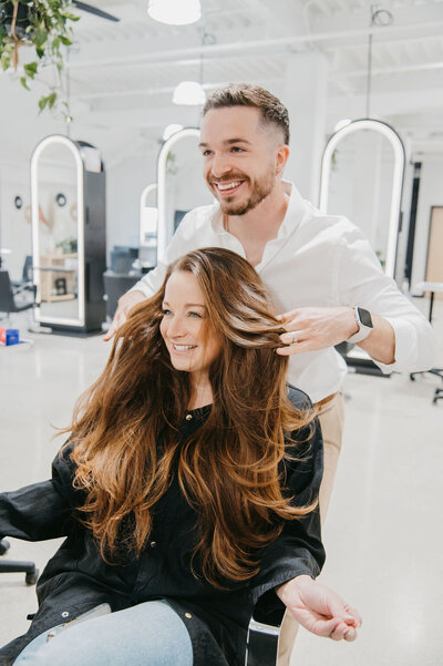 Hair stylist showcasing long, voluminous hair extensions on a smiling client at Salon Beau.
