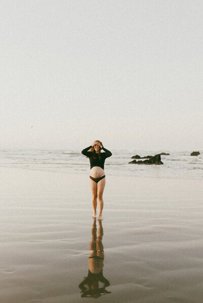 An expectant mother walking along a beach and running her hands through her hair during a maternity photoshoot with lucy jane photography