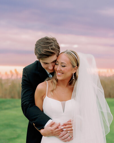 A couple hugs one another while the sun sets behind them.