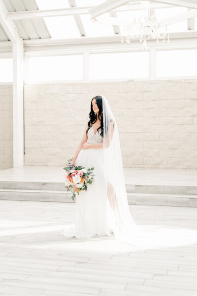 bride with a two piece wedding dress holding a bouquet with eucalyptus orange and pink flowers with a cathedral length veil