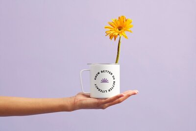a hand holding a white mug with a daisy in it