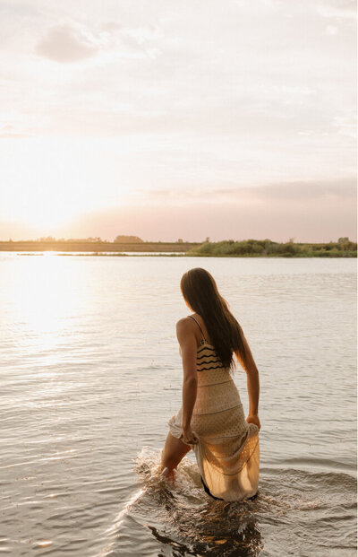 Girl walking away from the camera in a lake at sunset.
