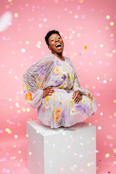 Capture the essence of joy with this vibrant image of a Black woman laughing amidst falling confetti. A perfect representation of celebration and happiness, showcasing radiant beauty and carefree spirit.