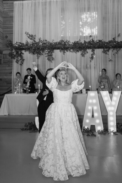Bride and groom walks into their wedding reception while the bride signals a heart hand