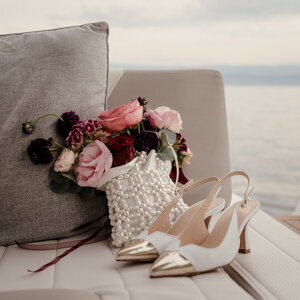 Photo de détail à bord d’un bateau sur le Lac Léman en Suisse : le sac haut de gamme de la mariée, son bouquet et ses chaussures Jimmy Choo – une scène élégante captée dans l’intimité d’un mariage chic