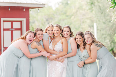 Bride and her bridesmaids hug close as they smile for a photo at Red Gate Farms