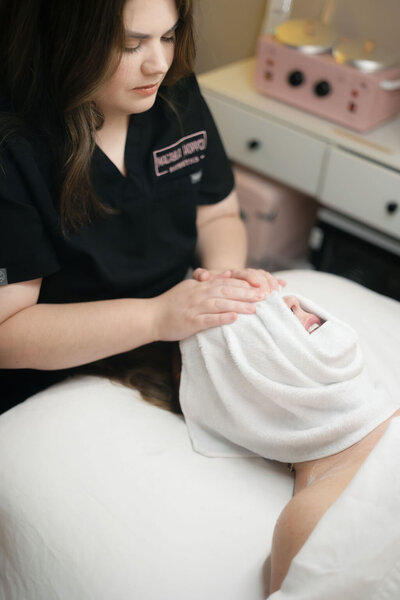Macayla Hopper wrapping warm towel around clients face during skincare services in her studio in Hartselle, Alabama