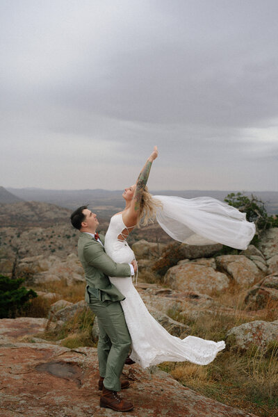 groom lifting bride up while her veil flows in the wind